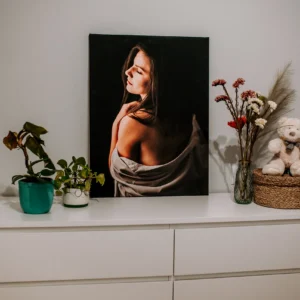 Fotoobraz z portretem kobiety z nagim ramieniem na czarnym tle ustawiony na białej komodzie