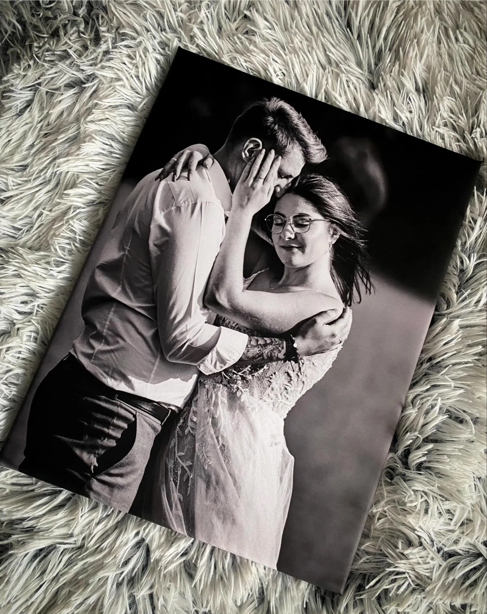 Czarno-biały fotoobraz przedstawiający zakochaną parę w objęciach na tle dywanu.